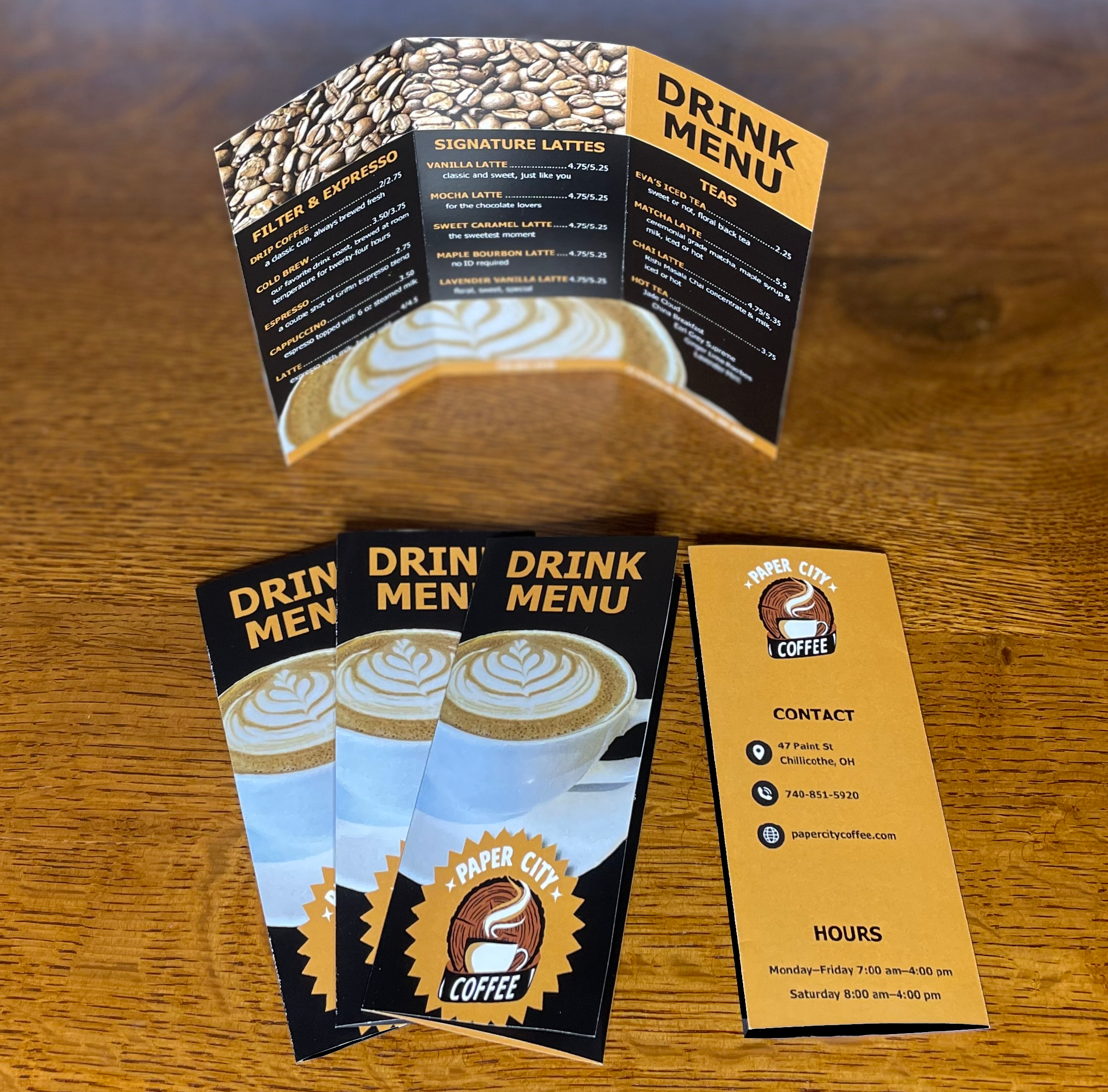 Portfolio Flyers & brochures. 3-fold brochures, black and light brown background. Drink menu on inside. Photo of a cappucino and Paper City logo on front. Logo and contact info on back.